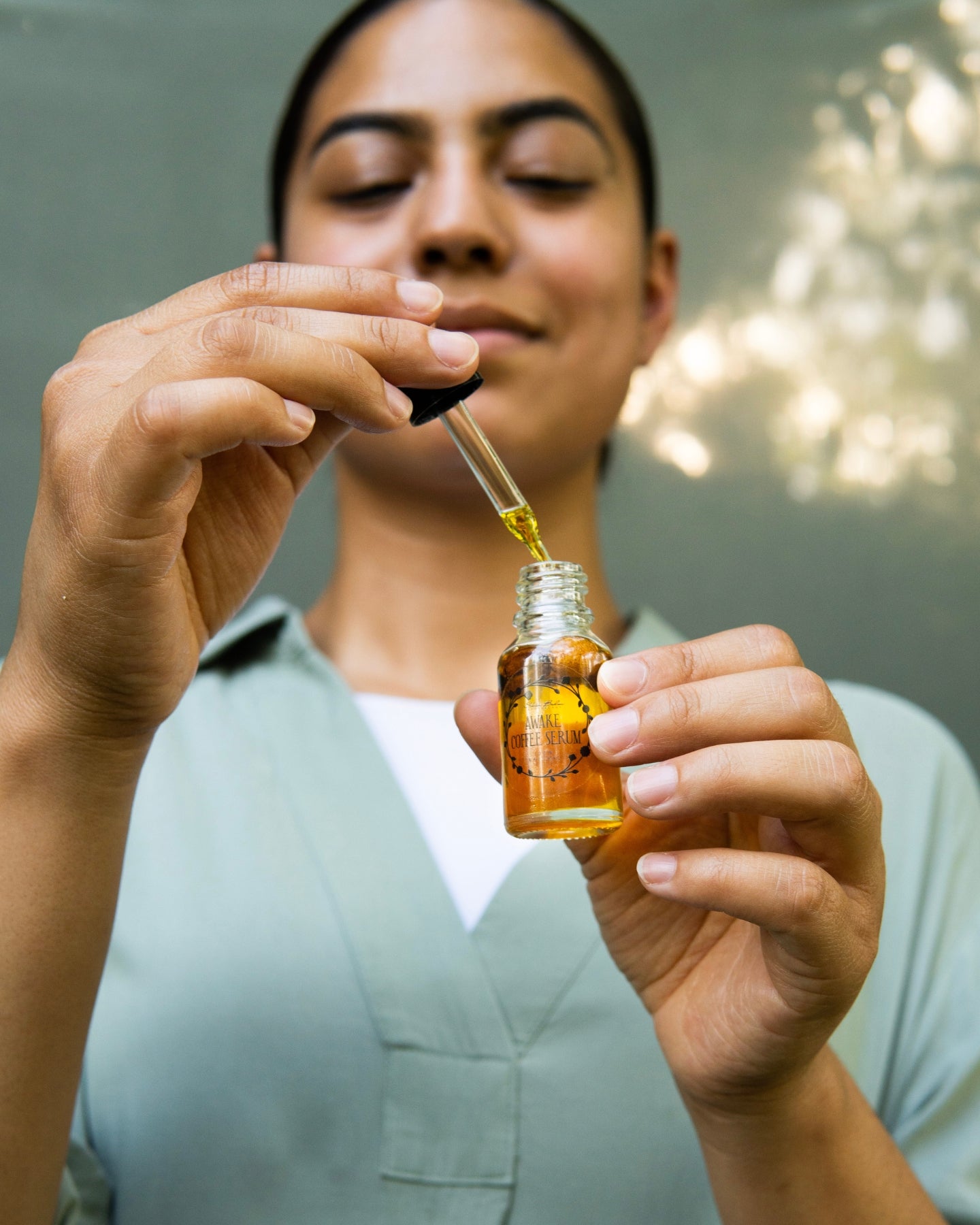 A close-up shot of a woman removing the dropper from the Awake Coffee Serum.