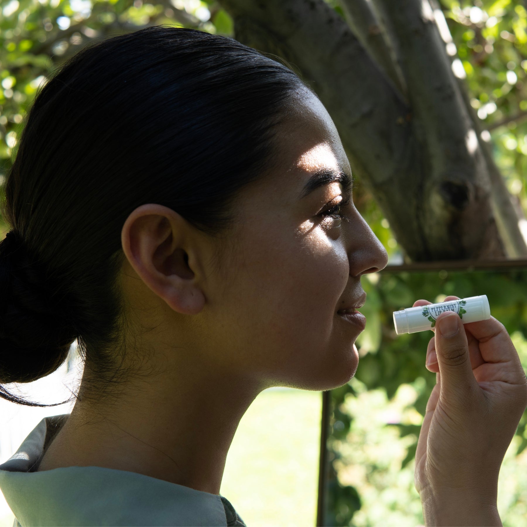 A profile view of a woman applying the Peppermint Lip Balm to her lips.