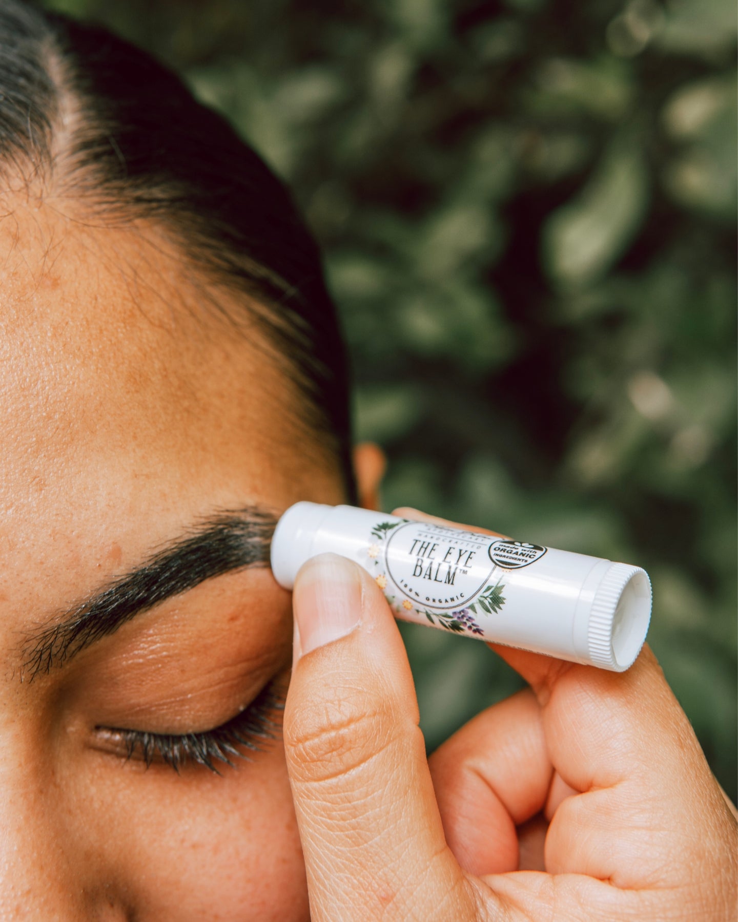 A close-up shot of a woman applying The Eye Balm™ to her eyebrows.