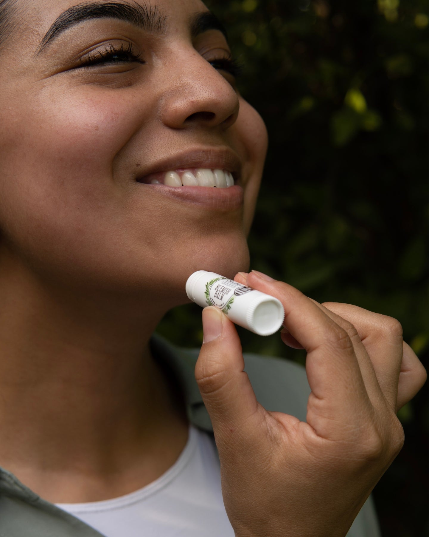 A close-up shot of a smiling woman applying the Blemish Balm on her chin.
