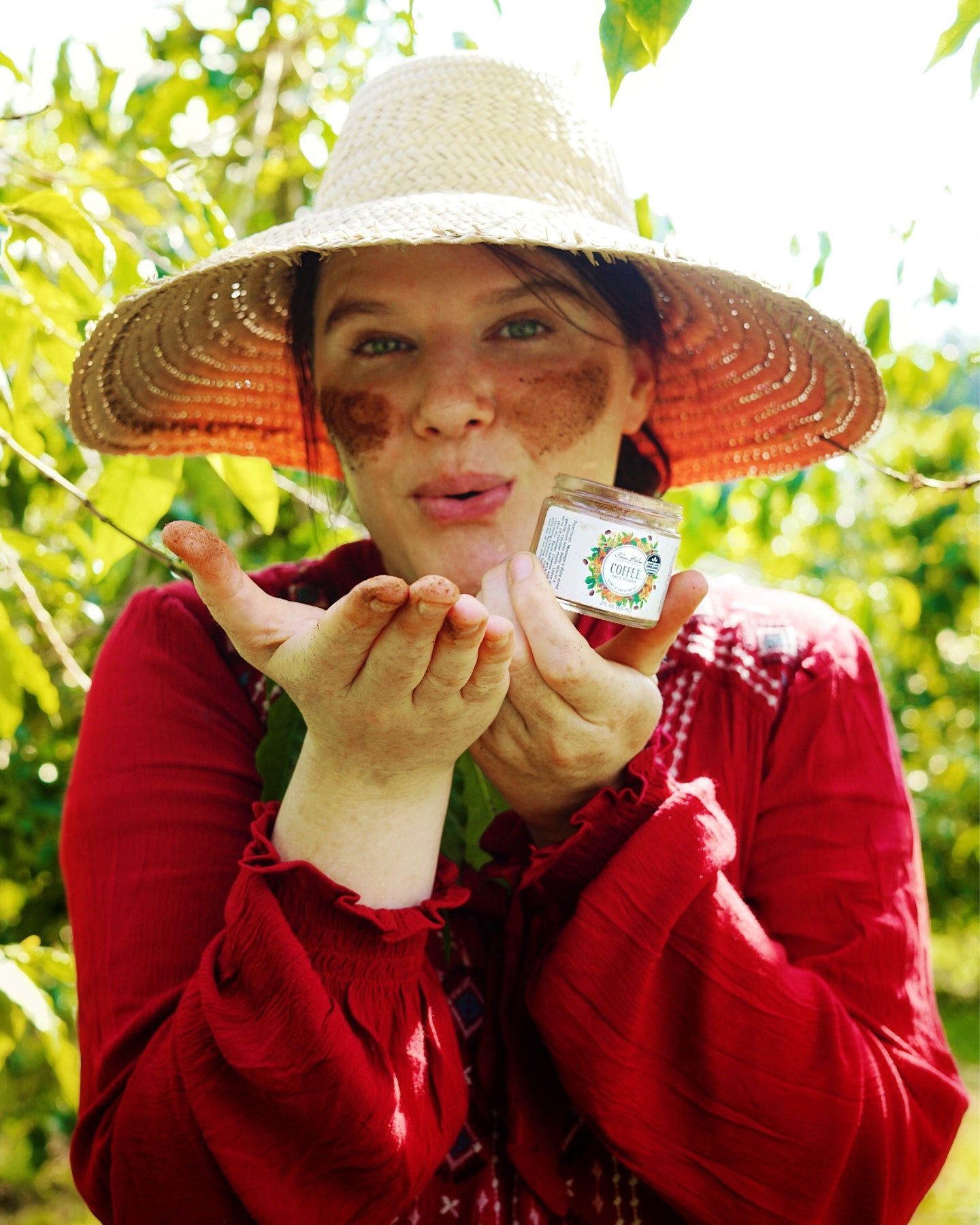 A woman standing in a field of coffee trees holding a jar of Coffee Face Polish.