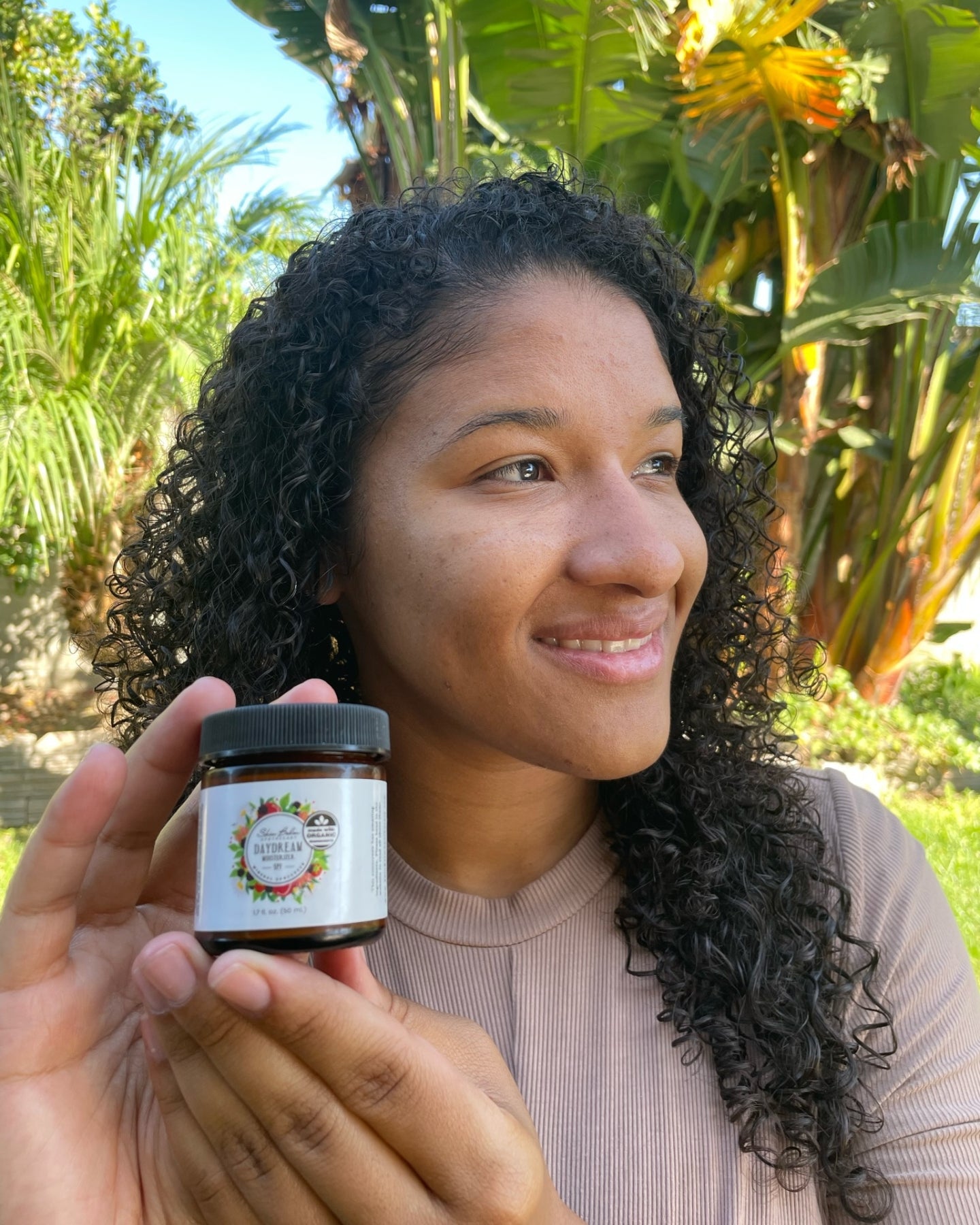 A smiling woman holds a jar of Daydream Mineral Sunscreen.
