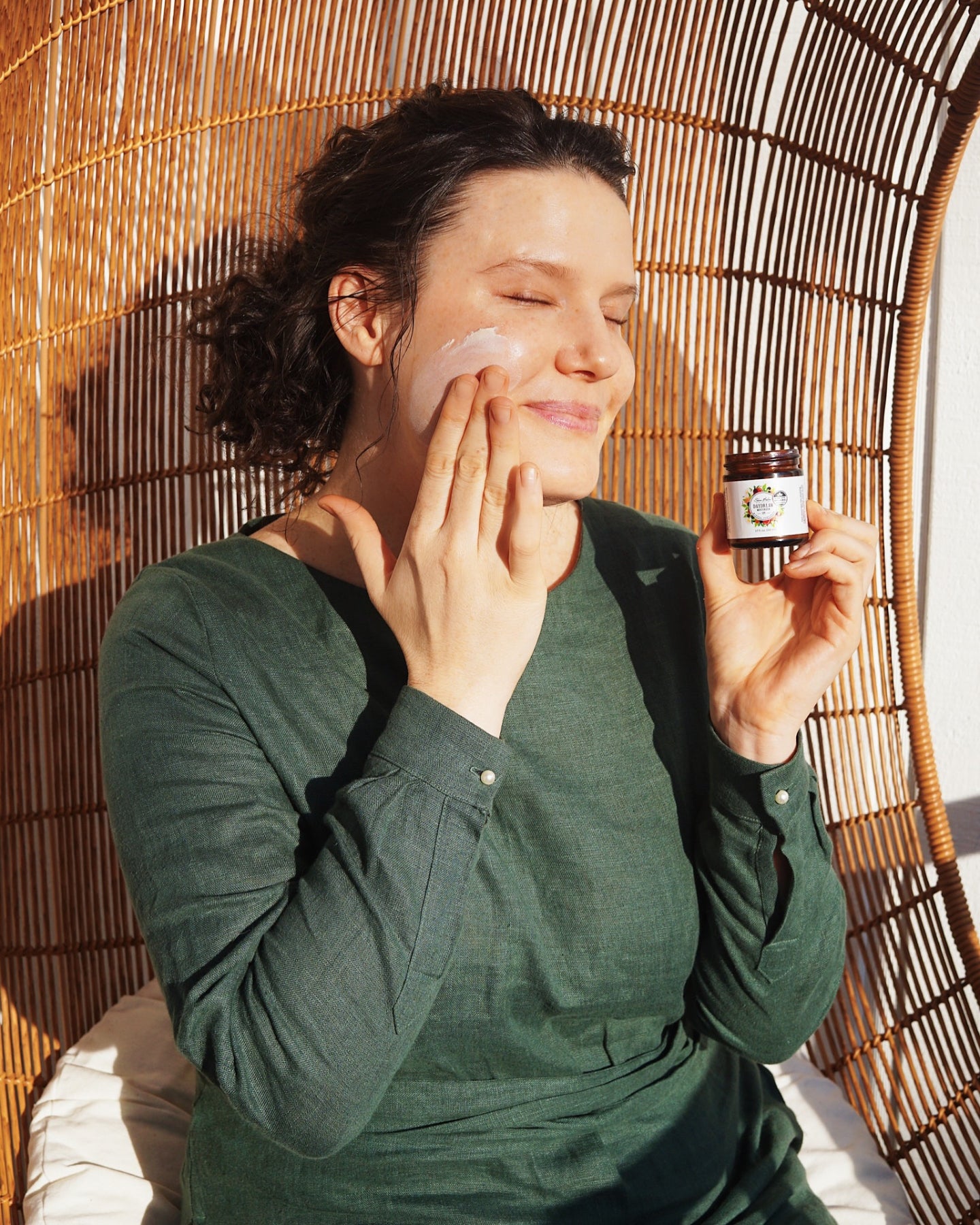 A smiling woman applies Daydream Mineral Sunscreen to her face in the sun.