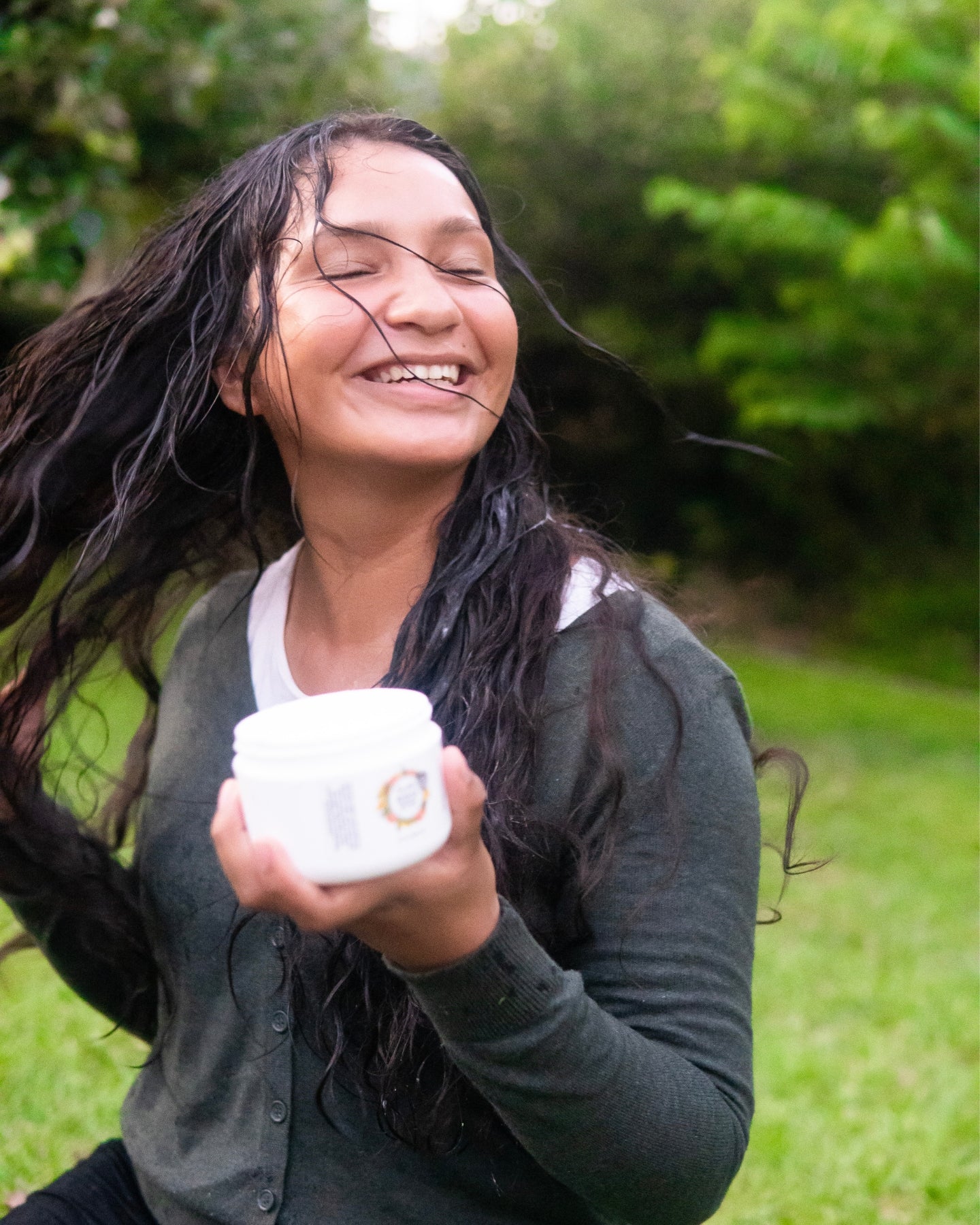 A smiling woman twirls her hair as she holds a container of Nourish Conditioner.
