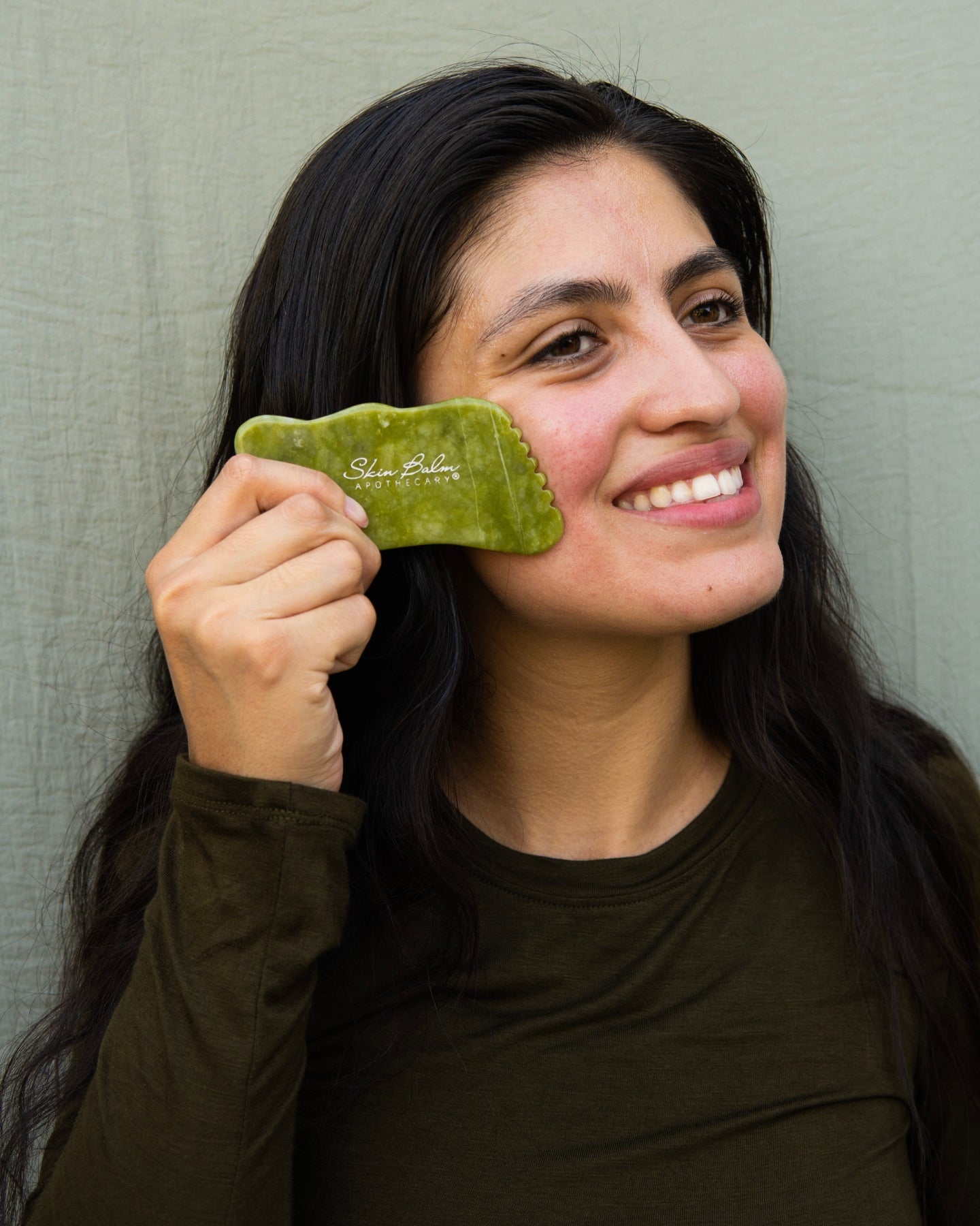 A smiling woman uses the Jade Facial Stone on her face.