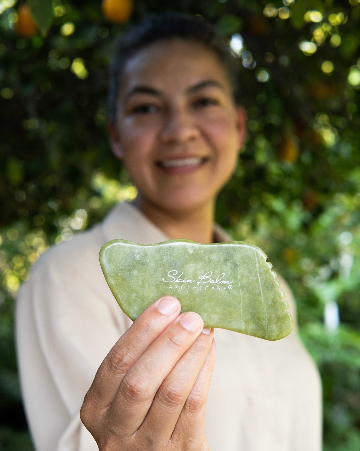 A close-up shot of the Jade Facial Stone with a smiling woman blurred in the background.