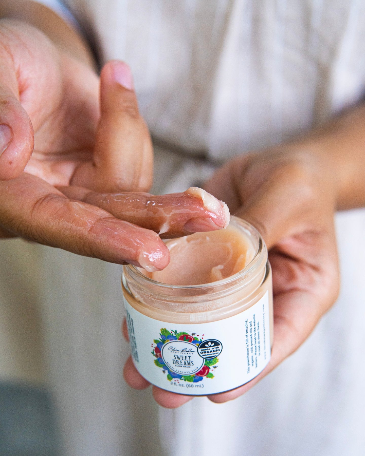 A close-up shot of a woman scooping the Sweet Dreams Glow Balm out of the jar with her fingers.