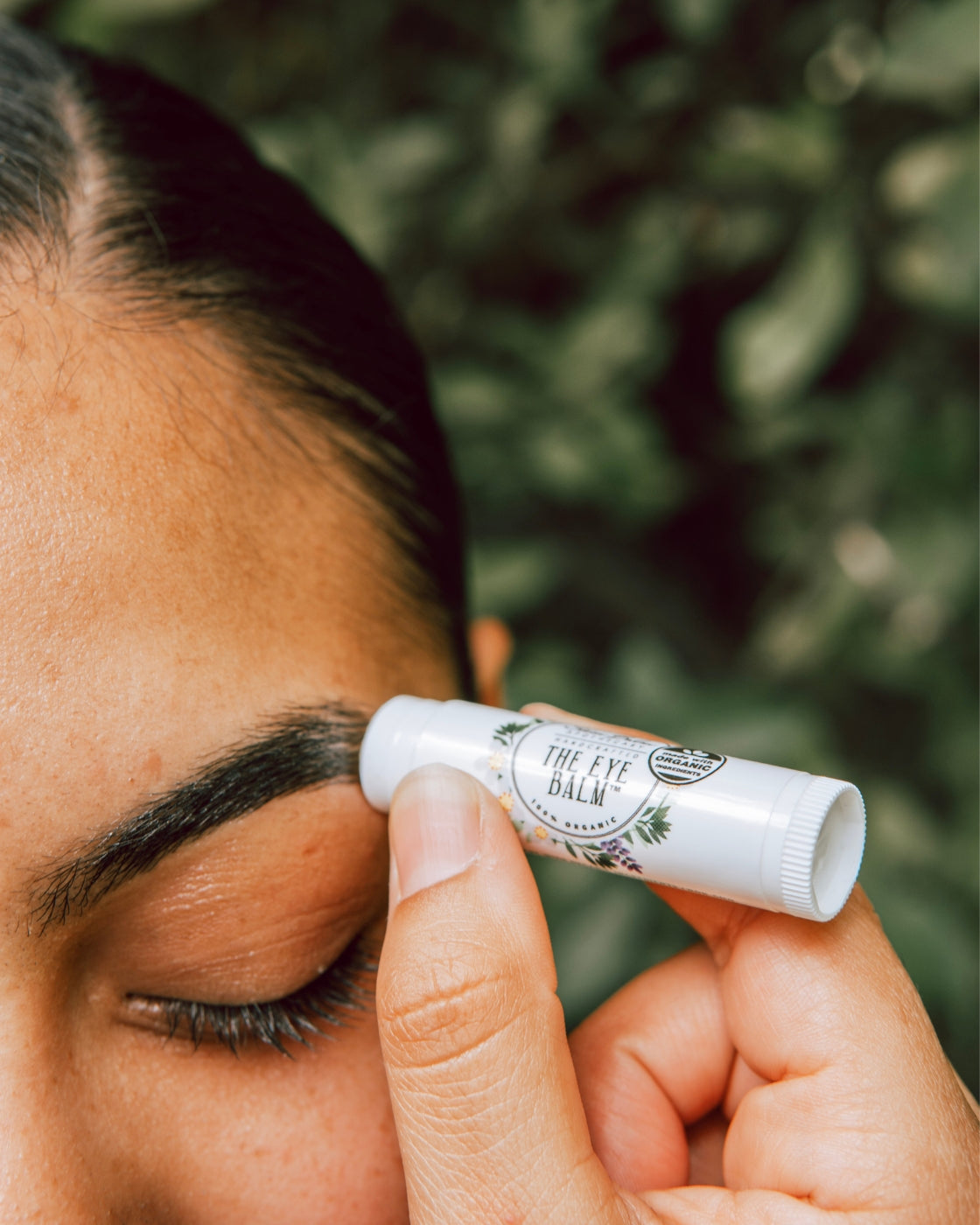 A close-up shot of a woman applying The Eye Balm™ to her eyebrows.